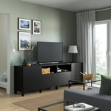 Modern living room with flat-screen tv on BESTÅ unit, coastal prints, lamp, glass coffee table, gray couch, and sliding glass door.