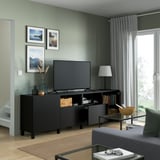 Green living room, black tv stand with flat screen, photos, lamp, and glass coffee table with wooden bowl.