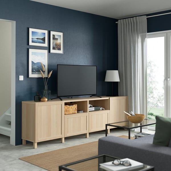 Modern living room with flat-screen tv on BESTÅ bench, gray sofa, coffee table, dark blue walls, large window.