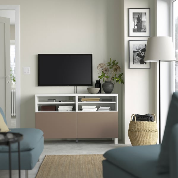 Minimalist living room: light green walls, soft lighting, large tv on BESTÅ bench, decor, blue chair, basket.