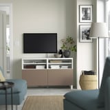 Minimalist living room: light green walls, soft lighting, large tv on BESTÅ bench, decor, blue chair, basket.