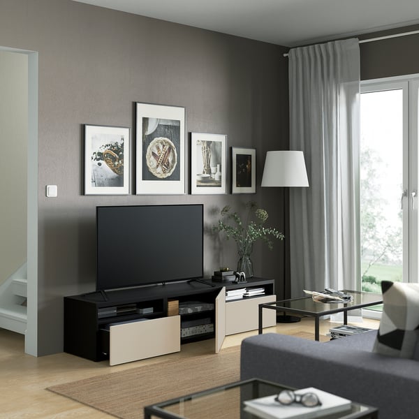 Modern living room with black tv bench, gray wall, framed pictures, large window, cozy sofa, and glass coffee table.