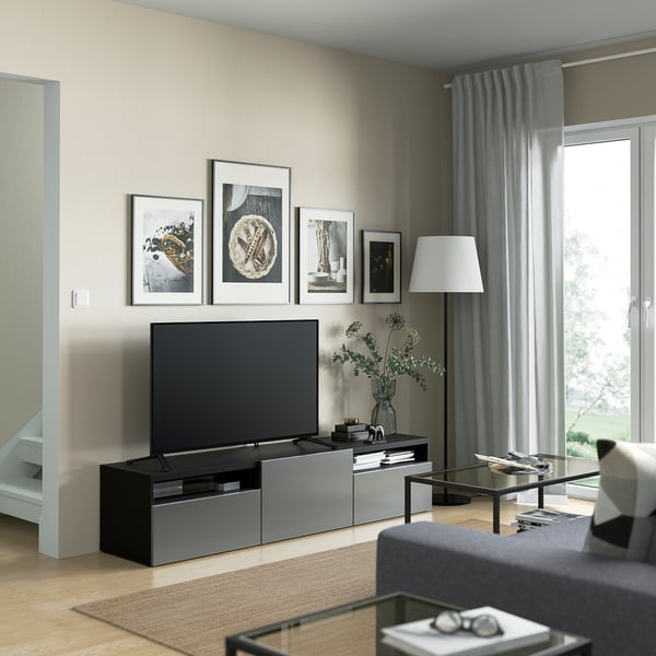 Modern living room with BESTÅ tv bench, flat-screen tv, framed art, gray curtains, floor lamp, and green plant.