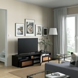 Modern living room with BESTÅ tv bench, flat-screen tv, framed art, and large window. Include cable management and adjustable feet for stability.
