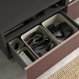 Open BESTÅ tv bench drawer showing organized gaming controllers, headphones, and remotes with cable management.
