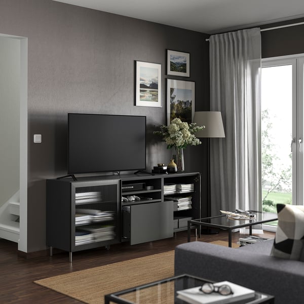 Modern dark grey living room with BESTÅ tv stand, flat screen tv, grey curtains, large window, rug, coffee table, and decorative flowers.