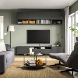Modern living room with black BESTÅ tv bench, grey couch, round coffee table, flat screen tv, and wall cabinets.