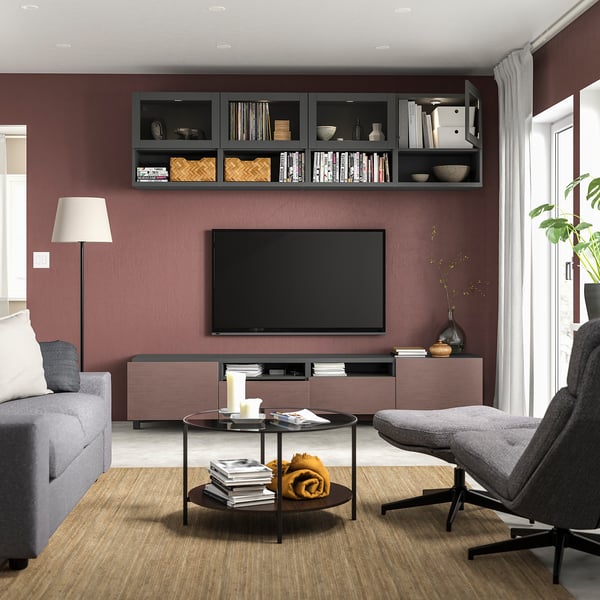 Modern living room with maroon walls, grey furniture, flat-screen tv, coffee table, books, and plants.