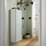 Modern light green BESTÅ storage unit. Tall, slim cabinet with two doors fits neatly in corner. Accented by black hardware and round wall lamp.