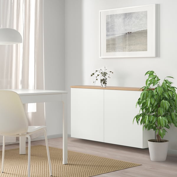 Modern BESTÅ storage unit with single cabinet, wood top, beach art, plants, and desk.