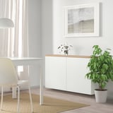 Modern BESTÅ storage unit with single cabinet, wood top, beach art, plants, and desk.