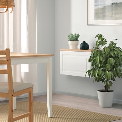 A minimalist dining room with BESTÅ sideboard, plant, and light wooden chairs around white wall-mounted table.