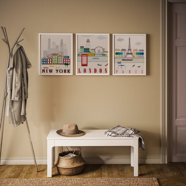 Three city prints: new york, london, paris on beige wall; white bench with hat and scarf; coat rack with jackets.