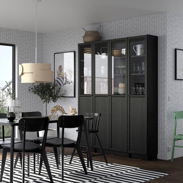 Dining room with BILLY bookcase displaying glassware and dishes, flanked by pictures, modern chairs, and striped rug.