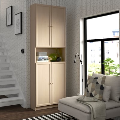 Modern living room with tall, light-colored BILLY bookcase, patterned wallpaper, grey sofa, and city view window.