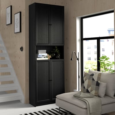 Modern living room with black BILLY bookcase, gray couch, large window, white stairs, black & white rug, and green plant.