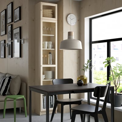 Modern dining area with black table, BILLY bookcase, pendant light, green stool, sofa, and city view.