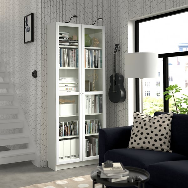 Modern living room with BILLY white bookcase, black couch, large window, guitar wall mount, and stylish decor.