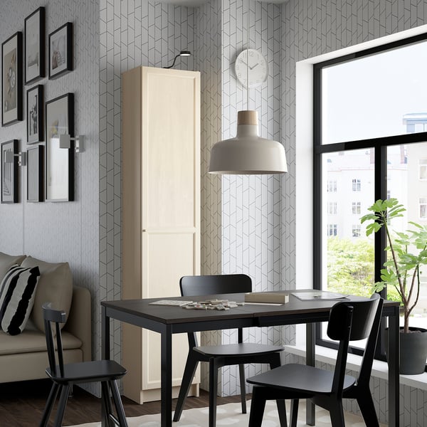 Modern dining room with BILLY white bookcase, black table, chairs. Stylish pendant lamp, large window, geometric walls, cozy cushioned couch.