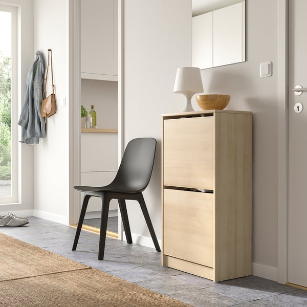Wooden shoe cabinet beside door, with lamp, bowl, and coats.