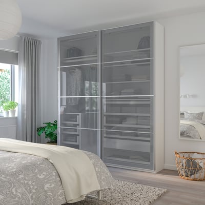 BJÖRNÖYA wardrobe with glass doors, hangers, and shelves next to bed.