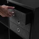 Hand opens black fabric drawer with metal ring handle, part of BLÄDDRA storage unit.