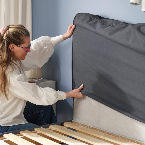 Woman putting on BLÅFJÄLLET bed cover, machine washable for clean, fresh comfort.