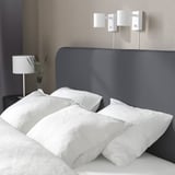 A minimalist bedroom with a gray bed, white pillows and a modern lamp.