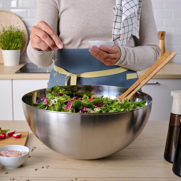 Person preparing salad. Large stainless-steel bowl used for mixing greens.