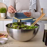 Person preparing salad. Large stainless-steel bowl used for mixing greens.
