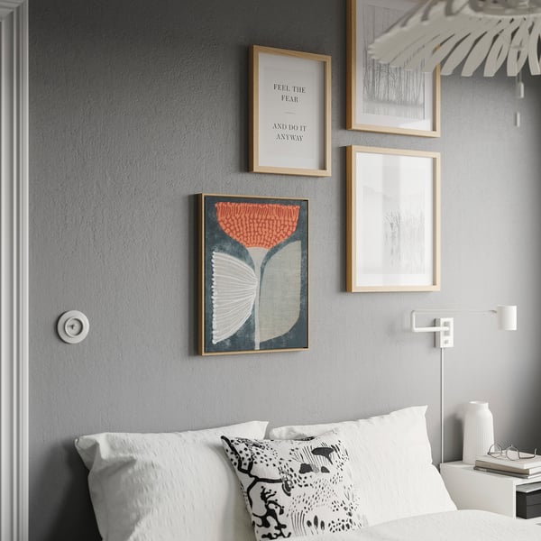 Modern bedroom with colorful BLODFLÄDER poster. Three framed prints on grey wall, bed with white pillows, pendant light.