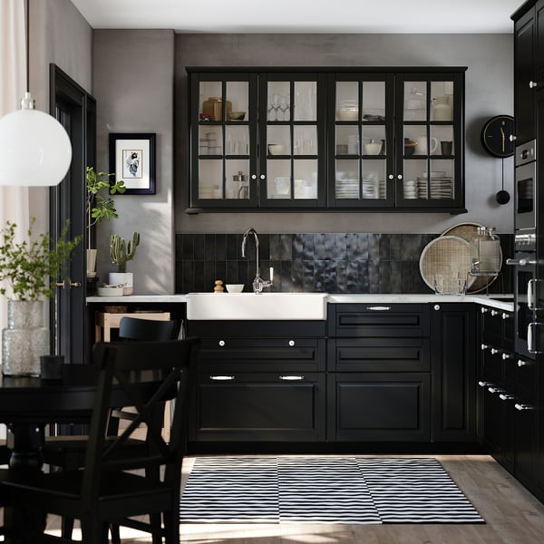 Modern black kitchen with glass cabinets, black sink, and striped rug. Sleek design with dark wood and metallic backsplash.