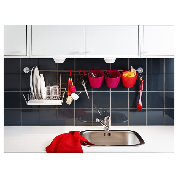 Modern kitchen sink in stainless steel, with hanging utensils, cups, and red towels on dark blue tiled wall.