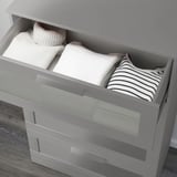 Grey chest of drawers with frosted glass top drawer, partially open revealing neatly folded clothes.