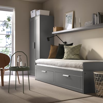 Modern, grey BRIMNES day-bed. Cool-toned room with wooden chair. Efficient storage, fits small spaces.