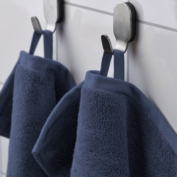 Two navy blue towels hang on black and silver wall hooks. The thick, absorbent towels have a textured pattern and are secured with loops.