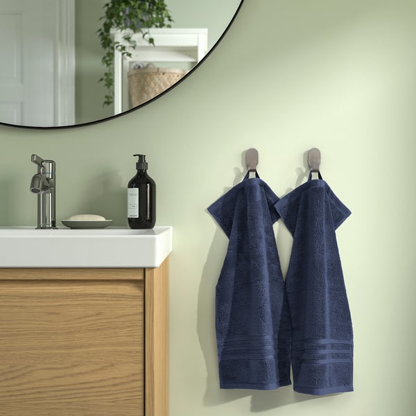 Blue BROKGLIM towels on hooks next to modern vanity with sink, soap, and mirror. Organic cotton, absorbent, decorative border.