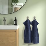 Blue BROKGLIM towels on hooks next to modern vanity with sink, soap, and mirror. Organic cotton, absorbent, decorative border.
