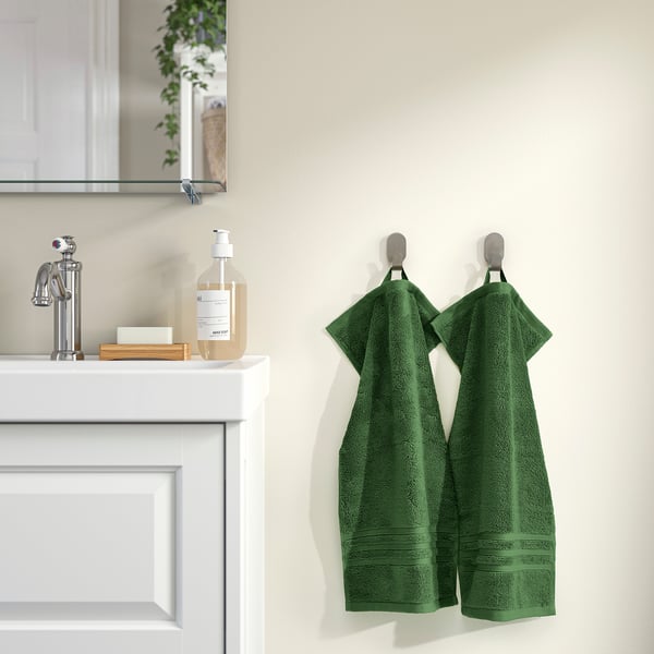 Two green BROKGLIM towels hang on hooks beside a white bathroom vanity, adding color and elegance.