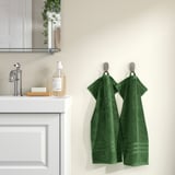 Two green BROKGLIM towels hang on hooks beside a white bathroom vanity, adding color and elegance.