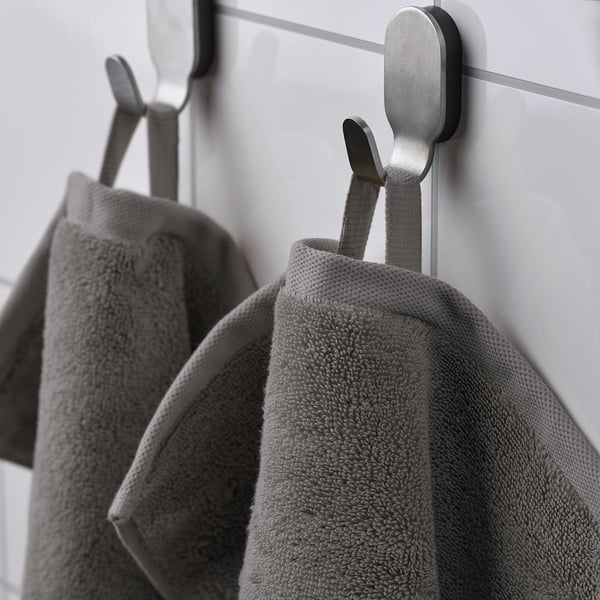 Two grey towels hang on metal hooks; one displays a woven border and both show dense terry texture, indicating absorbency.