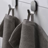 Two grey towels hang on metal hooks; one displays a woven border and both show dense terry texture, indicating absorbency.