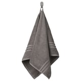 A gray BROKGLIM towel hangs neatly on a hook, showcasing an elegant woven border. Made of organic cotton, it offers a soft, absorbent texture.