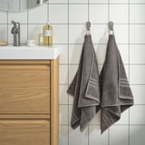 BROKGLIM grey towels hang neatly in modern bathroom. Soft, absorbent organic cotton, coordinated with sleek decor.