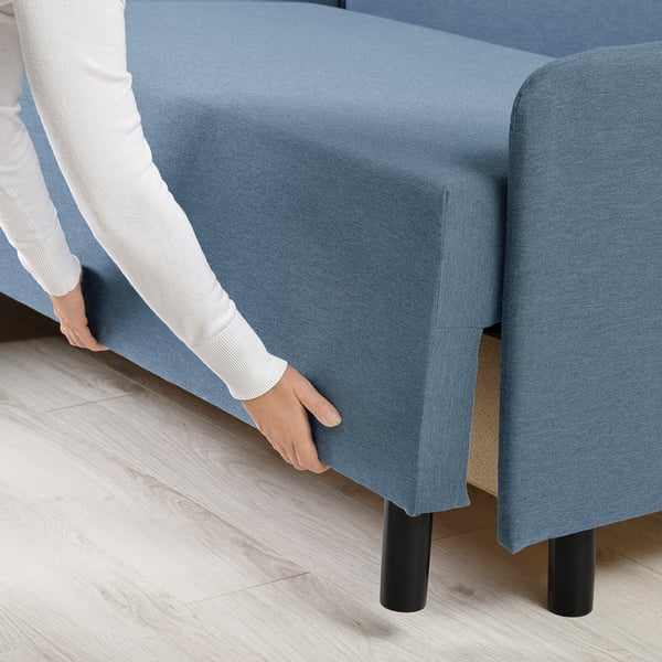 Person adjusting cushions on blue sofa-bed.