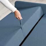 Hand pulling out blue sofa-bed cushion, revealing internal storage. Modern, convertible design for comfort and space efficiency.