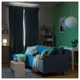 Cozy living room with blue BRUKSVARA l-shaped sofa-bed, colorful pillows, gray curtains, green wall, and white desk.