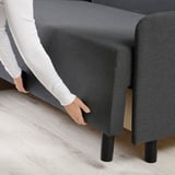Person adjusting grey sofa-bed with black legs, demonstrating easy conversion and accessibility of hidden storage.