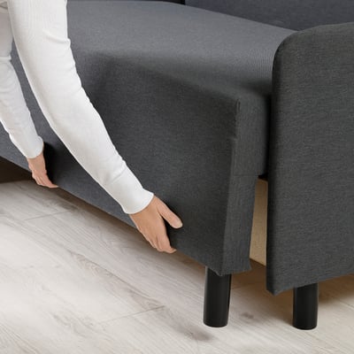 Person adjusting grey sofa-bed with black legs, demonstrating easy conversion and accessibility of hidden storage.