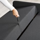 Hand pulls out compartment on a gray sofa-bed, showcasing its built-in storage feature.
